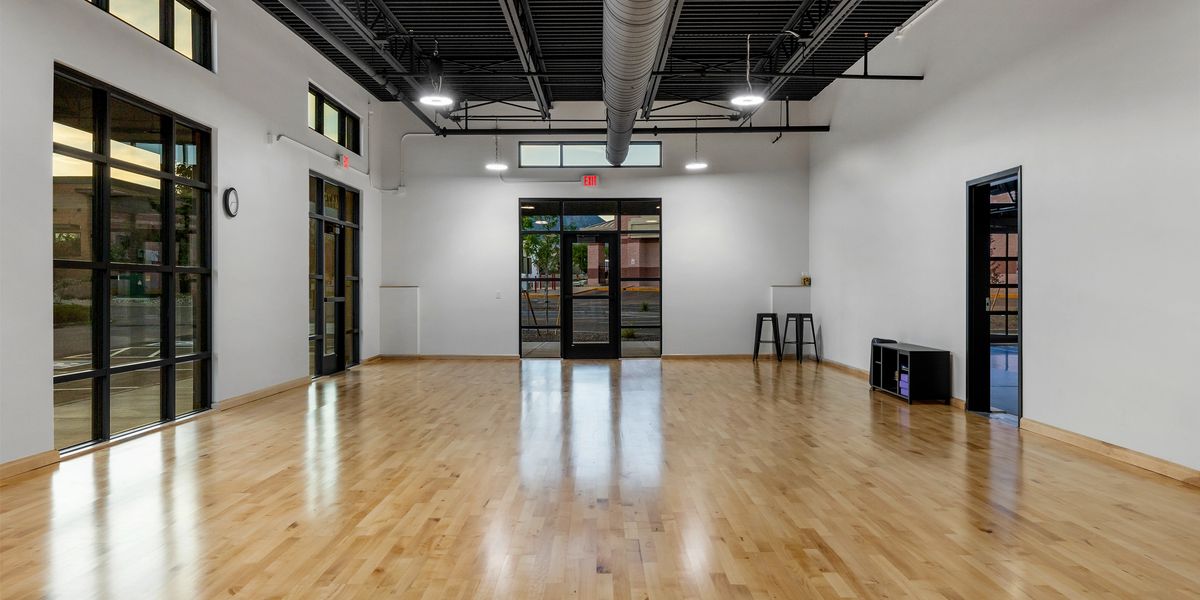 A smaller studio with wood paneled floors, windows, chairs, and storage space.