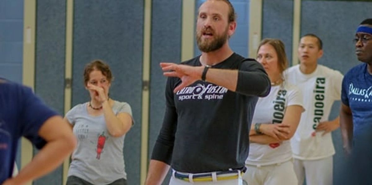 An adult man teaching his capoeira students discipline. 
