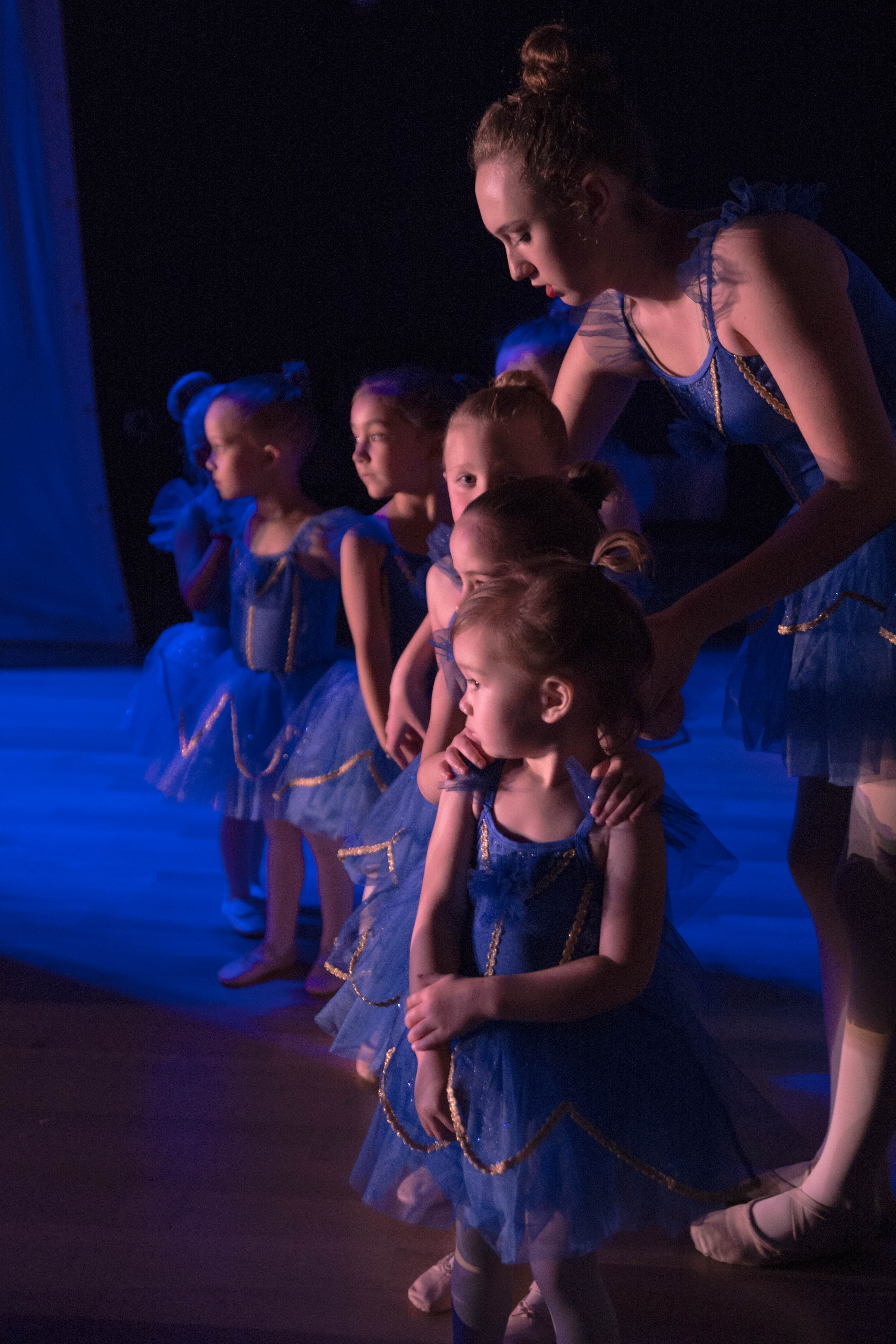 photo of a teenage dance assistant helping preschool students prepare to go onstage for a recital performance