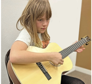 8 year old girl looking down on music playing music with a guitar